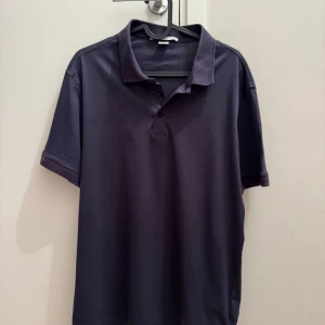 Mörkblå pikétröja Tiger of Sweden - Snygg mörkblå pikétröja från Tiger of Sweden med klassisk krage och knappar framtill. Tillverkad i mjuk bomull och har korta ärmar. Perfekt för en clean och stilren look. Krage och ärmar är lite slitsa men i övrigt är den i bra skick. Nypris 1200 :-