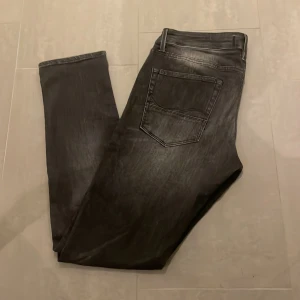 Svarta slim jeans Slim/Glenn - Säljer ett par svarta jeans från Slim/Glenn med snygg tvättad look. Jeansen har klassisk femficksdesign, smal passform och normal midja. Materialet är jeans och färgen är mörksvart med lätt slitningseffekt. Perfekta för dig som gillar en stilren och modern vibe. Jack and Jones!
