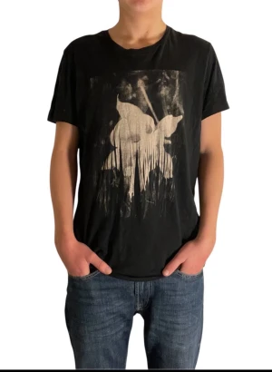 Svart t-shirt från Hugo boss - Cool svart t-shirt med ett stort, konstnärligt tryck i vitt på framsidan. T-shirten har rund hals och korta ärmar, perfekt för en avslappnad och trendig look. Passformen är normal och materialet känns mjukt mot huden. Modellen är 177cm
