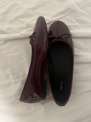 Vinröda lackballerinaskor från Nelly - ALDRIG ANVÄNDA, HELT NYA🫶Snygga vinröda ballerinaskor i glansigt lackmaterial från Nelly. Skorna har rund tå, liten rosett framtill och låg klack. Perfekta för dig som vill ha en stilren och trendig look. 