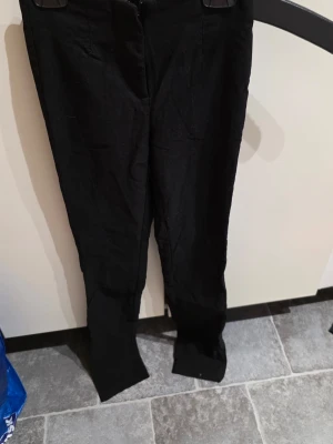 Svarta kostymbyxor med smal passform - Snygga svarta kostymbyxor med smal passform och klassisk design. Byxorna har diskreta fickor framtill och dragkedja. Perfekta till en stilren look och passar till många olika outfits.