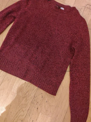Mörkröd stickad tröja - Mysig mörkröd stickad tröja med rund halsringning och långa ärmar. Tröjan har en lätt melerad struktur och ribbstickade muddar vid ärmslut och nederkant. Perfekt för kyliga dagar och enkel att matcha med jeans eller kjol.
