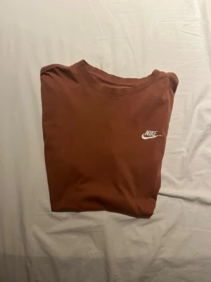 Brun Nike t-shirt med logga - Säljer en brun t-shirt från Nike med klassisk vit logga på bröstet. T-shirten har rund hals och korta ärmar. Perfekt för en avslappnad och sportig stil. Storlek L, passar M.
