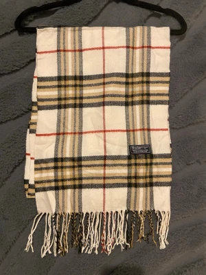 Klassisk Burberry Halsduk - Burberry halsduk 🤍  Klassisk Burberry-halsduk i det välkända rutmönstret. En tidlös favorit som aldrig går ur stil.  ✨ Detaljer: – Material: Lammull – Färg: Vit/Röd/Biege/Svart – Mått: 170 cm x 32 cm – Skick: Mycketbra – Original: ja  Perfekt till höst & vinter och funkar både casual och uppklätt. Skickas snabbt 📦  Pris kan diskuteras.