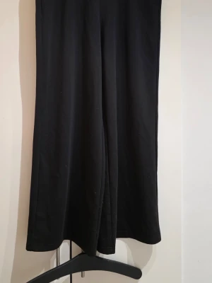 Svarta vida mjukisbyxor - Säljer ett par svarta mjukisbyxor med rak och vid passform. Byxorna har resår i midjan och är gjorda i ett mjukt och stretchigt material, perfekt för chill dagar. Inga synliga loggor eller detaljer, enkel och clean look.