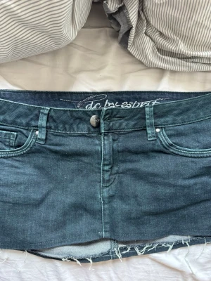 Mörkblå jeanskjol från Esprit - Trendig mörkblå jeanskjol från Esprit med rå kant nertill och klassiska femficksdetaljer. Kjolen har knapp och dragkedja framtill samt bälteshällor. Perfekt för en avslappnad och cool stil. strl L men sitter mer spm M