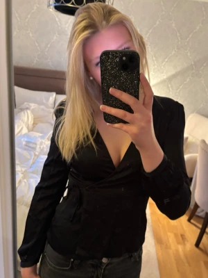 Svart Zara blus - Snygg svart omlottblus från Zara med v-ringning. Blusen har långa ärmar och knyts i sidan för en figurnära passform🤍