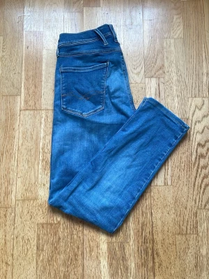 Blå slim jeans från Replay - Snygga blå jeans från Replay med klassisk femficksdesign och kontrastsömmar. Jeansen har en slim passform och är tillverkade i bomull med en liten mängd stretch för extra komfort. Perfekta för en avslappnad och trendig look.
