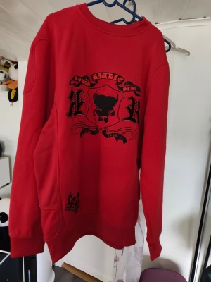 Röd crewneck från Richle med tryck - Röd sweatshirt från Richle med svart tryck framtill och en krona vid nederkanten. Tröjan har rund halsringning och långa ärmar. Perfekt för dig som gillar streetwear och vill sticka ut med en cool design. Är mer som xl oversized eller xxl med smalare midja  👍