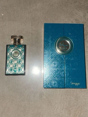 Siada Eau de Parfum från Zimaya - Lyxig parfym från Zimaya i en elegant turkos och guld dekorativ flaska med matchande ask. Flaskan har metalliska detaljer och ett mönstrat motiv som ger en exklusiv känsla. Perfekt för dig som vill sticka ut med en unik design på parfymhyllan. Dupe på god of fire. Parfymen är endast testsprayad.
