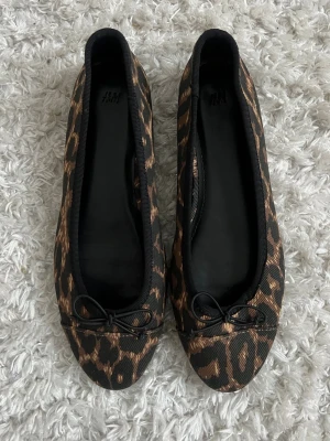 Ballerinaskor 🤎 - Snygga nya ballerinaskor i storlek 37 från H&M med leopardmönster i svart och brunt. Skorna har rund tå och en liten rosett framtill 🤎