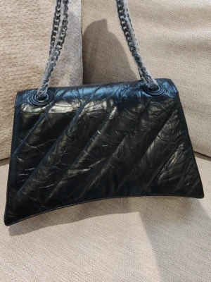 Svart quiltad handväska Balenciaga - Snygg svart handväska från Balenciaga i quiltat läder med diagonal sömnad. Väskan har en stilren B-logga framtill och kedjehandtag i silverfärg. 