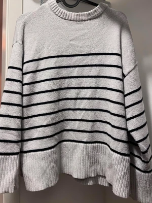 Vit stickad tröja med svarta ränder - Säljer en oversized vit stickad tröja i storlek L, dock har jag råkat tvätta den i varmt vatten så den har krympt lite och passar då för M istället. 