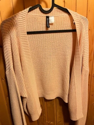 Ljusrosa kofta - Ljusrosa stickad kofta med öppen front och avslappnad passform. Koftan har ribbade muddar och är tillverkad i ett grovstickat material.