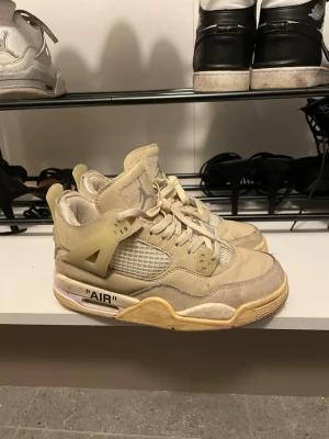 Off-White x Air Jordan 4 Sail - Exklusiva Off-White x Air Jordan 4 Sail sneakers i beige och krämvitt med meshpaneler, synliga sömmar och textdetaljen 'AIR' på sulan. Använda. Storleken är mer som 37
