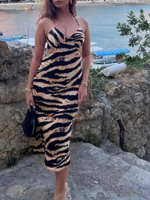 Zebramönstrad långklänning med smala band - Snygg långklänning med zebramönster i svart och beige. Klänningen har smala axelband, v-ringning och figurnära passform. Perfekt för dig som vill sticka ut med ett djurmönster och en trendig look.