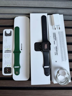 Apple Watch Series 5 44mm Space Gray 🔋 95% - Apple Watch Series 5 med 44mm boett i space gray aluminium. Kommer med svart sportarmband och extra grönt armband. Inkluderar originalförpackning, laddkabel och adapter. Modern design med fyrkantig skärm och smidiga silikonarmband.