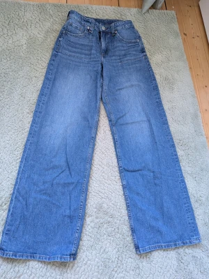 Blå wide leg jeans med hög midja - Säljer ett par klassiska blå jeans. Jeansen har fem fickor och stängs med knapp och dragkedja. Tillverkade i denim med en snygg tvättad look. Perfekta till en avslappnad stil och passar till det mesta.
