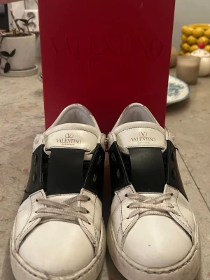 Valentino Opens Garavani vita sneakers - Snygga vita sneakers från Valentino Garavani med svart detalj över snörningen. Klassisk låg modell med rund tå och vita skosnören. Tillverkade i läder och kommer med originalpåse och box. Perfekta för dig som gillar exklusiv streetstyle. Kom gärna med bud! 