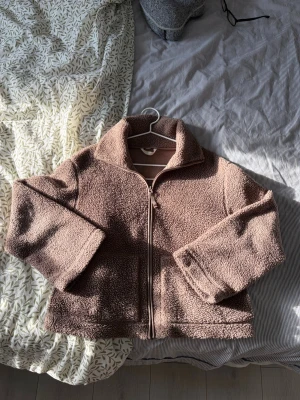 Brun teddyjacka med dragkedja - Mysig brun teddyjacka med hög krage och dragkedja framtill. Jackan har två stora fickor. Perfekt för våren och enkel att matcha med olika outfits. Har tyvärr dragit av lappen där strl står men är ganska säker på att den är i strl M. ☺️☺️