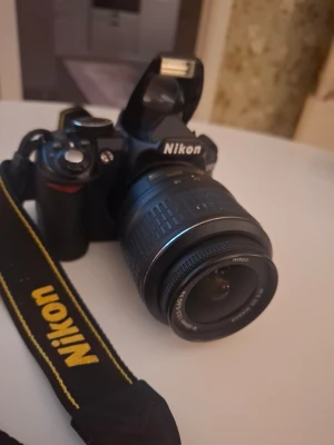 Nikon systemkamera med väska - Säljer en svart Nikon systemkamera med tillhörande objektiv och originalrem. Kameran har en klassisk design med tydliga reglage och inbyggd blixt. Medföljer gör en svart Nikon-väska i slitstarkt material med gul logga. Där är dock dragkedjan trasig men går att fixa Perfekt för dig som vill ta snygga bilder.