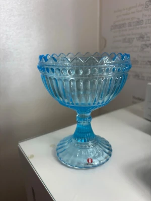 Blå glasskål på fot från Iittala - Snygg blå glasskål på fot från Iittala med dekorativt mönster och vågig kant. Perfekt som dessertskål eller till snacks. Den är oanvänd. 