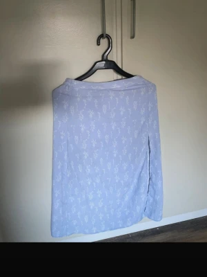 Ljusblå blommig kortkjol - Söt ljusblå kortkjol med vitt blommönster. Kjolen har en enkel och rak passform med resår i midjan för extra komfort. Perfekt för dig som gillar en feminin och avslappnad stil.  Använd en gång på skolavslutning, får tyvärr inte på den längre så kan ej ta bild