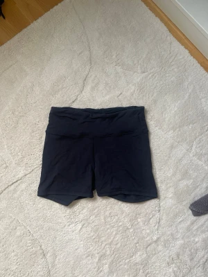 Svarta träningstights-shorts - Säljer ett par svarta träningstights-shorts perfekta för gymmet eller löprundan. Klassisk och enkel design med liten logga bak i midjan.