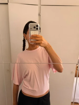 Ljusrosa croppad t-shirt - Säljer en ljusrosa croppad t-shirt med avslappnad passform och lite längre utsvängda ärmar. Perfekt till jeans eller mjukisbyxor för en chill look. Materialet känns mjukt och skönt mot huden. Aldrig använd. 