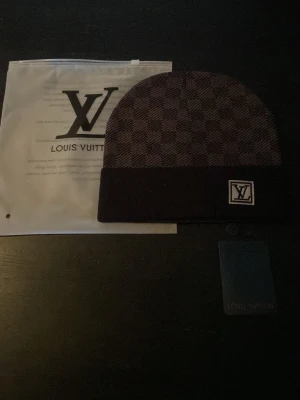 L&v mössa - Snygg svart mössa med klassiskt rutmönster och vikt kant. Mössan har. logga framtill och är tillverkad i mjukt material som passar perfekt för kyliga dagar. En stilren accessoar för dig som gillar exklusiva detaljer.