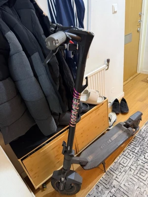 Svart el-scooter från Navee - Elektrisk scooter i svart från Navee med robust ram, bred fotplatta och stötdämpare bak. Utrustad med handtag, stöd och mönstrade däck. Perfekt för smidig transport i stan. Kommer med kvitto!