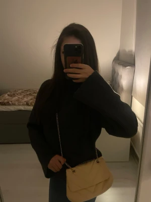 Beige quiltad handväska med kedja - Trendig beige handväska med quiltat mönster och snygg guldfärgad kedjerem. Väskan har en mjuk, vadderad look och stängs med lock. Perfekt för att lyfta din outfit med en stilren accessoar.