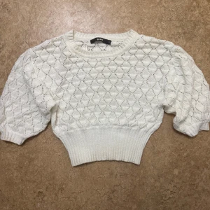Vit stickad tröja från Bik Bok - Superfin vit stickad tröja från Bik Bok med kort, croppad passform och bred ribbad midja. Tröjan har ett diskret rutmönster och puffiga trekvartsärmar som ger en trendig look. Perfekt att styla med höga jeans eller kjol. Storlek S, använd några få gånger. 