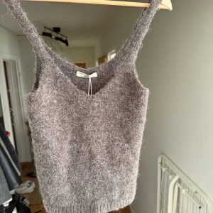Stickad brun linnetopp från Gina Tricot - Mysig stickad linnetopp från Reserved i brunmelerad färg. Toppen har v-ringning och breda axelband, perfekt för lager-på-lager eller som statement-piece. Materialet är fluffigt och ger en cool, avslappnad vibe.