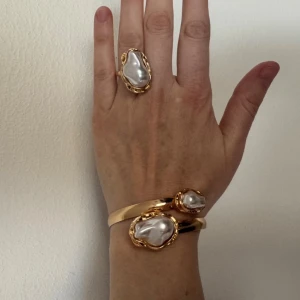 Armband och ring med pärldetaljer - Säljer ett set med ett guldigt armband och en matchande ring, båda med stora oregelbundna pärlliknande stenar. Snyggt statement-smycke med cool organisk form och lyxig känsla. Perfekt för dig som gillar unika accessoarer med lite extra bling.