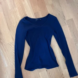 Marinblå ribbad långärmad topp XS - Säljer en marinblå långärmad topp i ribbat material med v-ringad hals. Sitter tight och har en enkel, stilren look som passar perfekt till jeans eller kjol. Superskön och stretchig modell för dig som gillar basic men ändå vill ha något snyggt.