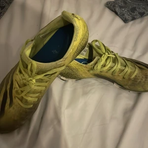 Gula Adidas fotbollsskor strl 41 1/3 - Säljer ett par gula Adidas fotbollsskor med klassiska svarta ränder på sidorna. Skorna har snörning och mönstrad sula med dobbar för bra grepp på planen. Ovandelen är i syntetmaterial och designen är sportig och smidig för snabba rörelser. Pris kan diskuteras😉