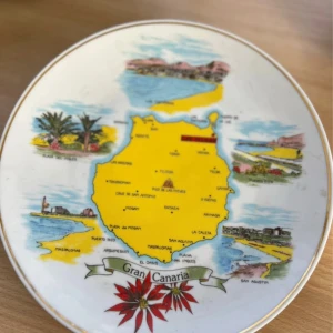 Gran Canaria souvenir-tallrik - Dekorativ souvenir-tallrik från Gran Canaria med karta och färgglada illustrationer av öns sevärdheter. Tillverkad av Macasa, utrustad med upphängningsanordning. Mindre spår av slitage på baksidan, annars i gott skick.