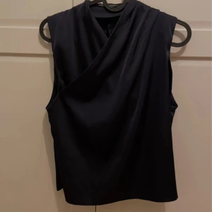 Omlottopp från Zara XS - Säljer en marinblå omlottopp från Zara i storlek XS. Toppen är ärmlös med snygg drapering framtill och har en stilren, elegant look. 