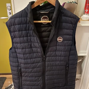 Mörkblå dunväst från Colmar - Snygg mörkblå dunväst från Colmar med quiltad design. Västen har två praktiska fickor med dragkedja och ett broderat Colmar-märke på bröstet. Perfekt för lager-på-lager och håller dig varm under kyliga dagar.