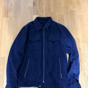 Mörkblå overshirt med dragkedja - Stilren mörkblå overshirt med klassisk krage, två bröstfickor med lock och dragkedja framtill. Jackan har raka ärmar och två snedställda fickor med dragkedja. Perfekt för lager-på-lager och enkel att matcha.