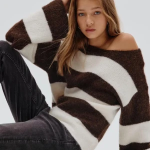 Randig brun och vit stickad tröja - Supermysig stickad tröja med breda bruna och vita ränder. Tröjan har en loose passform, lång ärm och en lite offshoulder-look. Perfekt för dig som gillar en chill och trendig vibe. Materialet känns fluffigt och mjukt mot huden.