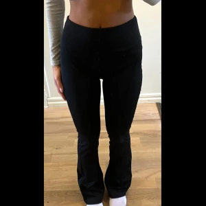 Svarta bootcut träningsleggings med hög midja - Snygga svarta bootcut träningsleggings med hög midja och figurnära passform upptill. Byxorna har ett stilrent och enkelt utseende utan synliga detaljer, perfekta för dig som gillar en clean look. Materialet är stretchigt och bekvämt.