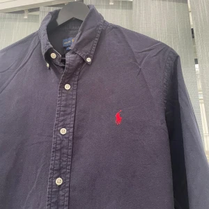 Skjorta Ralph Lauren - Snygg mörkblå skjorta från Ralph Lauren i slim fit-modell. Skjortan har klassisk krage, vita knappar och det ikoniska röda Polo-logot broderat på bröstet. Långärmad och tillverkad i mjuk bomull som känns skön mot huden.