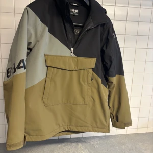 8848 Altitude vinterjacka  Scooter JR - Vindjacka från 8848 Altitude i svart, olivgrön och grått. Jackan har stor magficka med lock, huva och halv dragkedja framtill. Snyggt blockmönster och justerbara ärmslut med kardborre. Perfekt för dig som gillar stilren och sportig look.