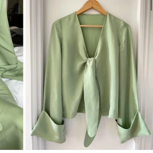 Ljusgrön omlottopp med knyt djerf avenue  - Säljer en ljusgrön omlottopp i glansigt material med långa vida ärmar och breda manschetter. Toppen har djup v-ringning och knyts framtill för en cool och avslappnad look. Perfekt att styla med matchande kjol eller jeans.