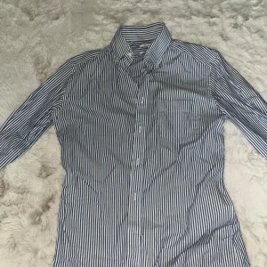 Randig slim fit skjorta från Reiss - Snygg skjorta från Reiss i slim fit-modell, med klassisk krage och knappar framtill. Skjortan har ett stilrent randigt mönster i marinblått och vitt, samt en bröstficka. Perfekt för dig som gillar en clean och modern look.