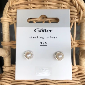 Örhängen pärla och cubic zirconia - Snygga örhängen från Glitter i sterling silver 925 med en rund vit pärla i mitten, omgiven av glittrande cubic zirconia-stenar. Perfekt för dig som gillar klassisk och elegant stil med lite extra bling. 9mm i diameter. 