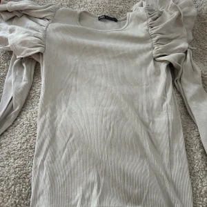 Beige ribbad topp med puffärm från Zara - Supersnygg ribbad topp från Zara i beige med långa puffärmar och rund halsringning. Tight passform som framhäver figuren. Använd en gång, tar frakt