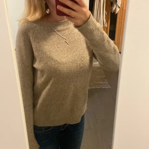 Beige stickad tröja med rund hals - Mysig beige stickad tröja med rund halsringning och långa ärmar. Tröjan har en enkel och stilren design, perfekt att matcha med jeans eller kjol. Ribbstickade muddar vid ärmslut och nederkant ger en snygg finish.